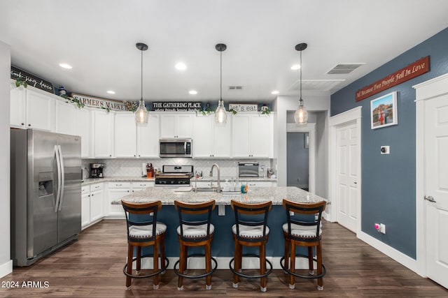 kitchen featuring dark hardwood / wood-style floors, pendant lighting, appliances with stainless steel finishes, a kitchen island with sink, and decorative backsplash