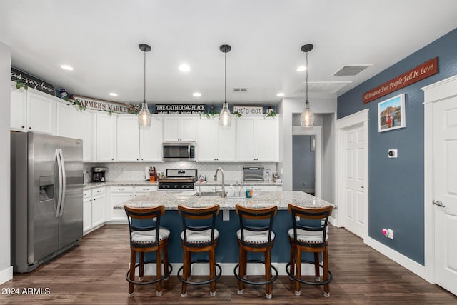 kitchen with an island with sink, white cabinetry, appliances with stainless steel finishes, and hanging light fixtures