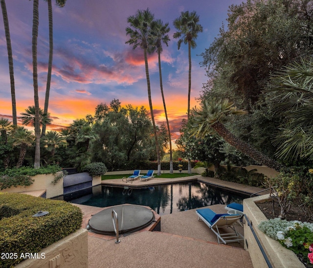 pool at dusk featuring a patio and an outdoor pool