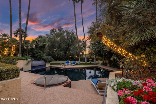 pool at dusk with an outdoor pool and a patio