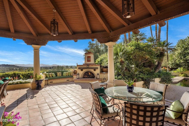 view of patio / terrace featuring a gazebo, a mountain view, a warm lit fireplace, and outdoor dining area