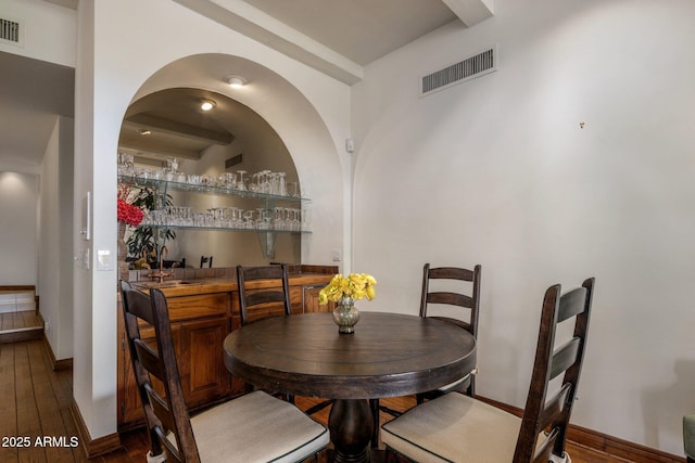 dining room featuring visible vents, wet bar, baseboards, and hardwood / wood-style flooring