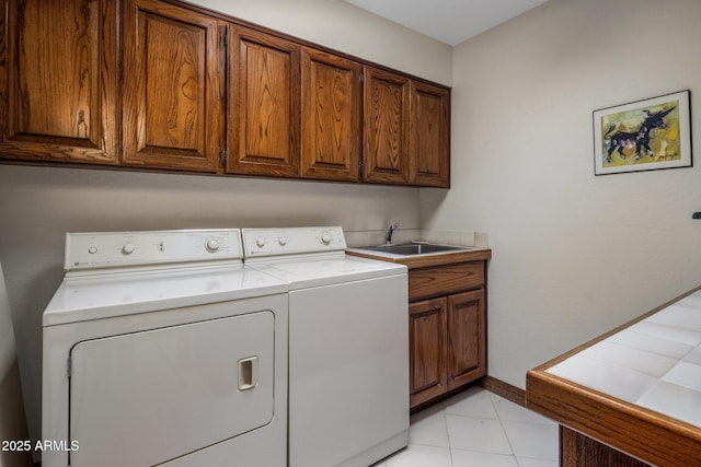 laundry area featuring baseboards, washing machine and dryer, light tile patterned floors, cabinet space, and a sink