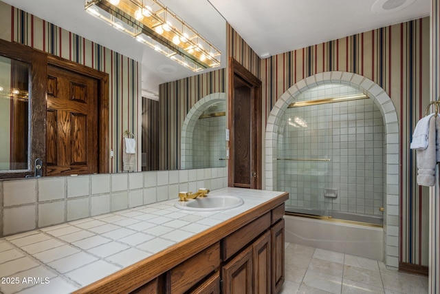 full bathroom featuring bath / shower combo with glass door, vanity, and wallpapered walls