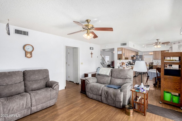 living room with ceiling fan, a textured ceiling, and light hardwood / wood-style flooring