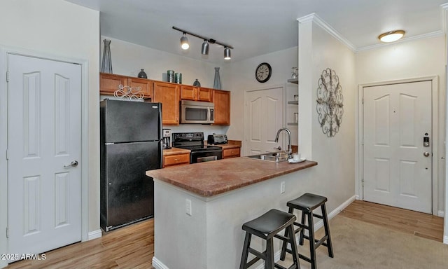 kitchen featuring brown cabinetry, light wood-style floors, a kitchen breakfast bar, black appliances, and a sink