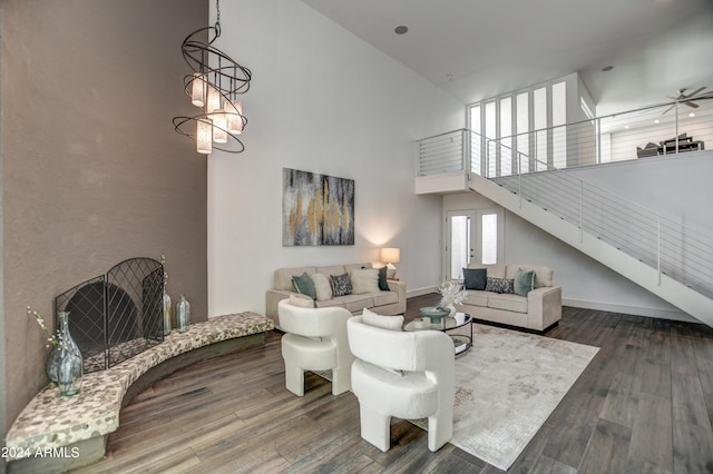 living room with ceiling fan with notable chandelier, dark hardwood / wood-style flooring, and a high ceiling