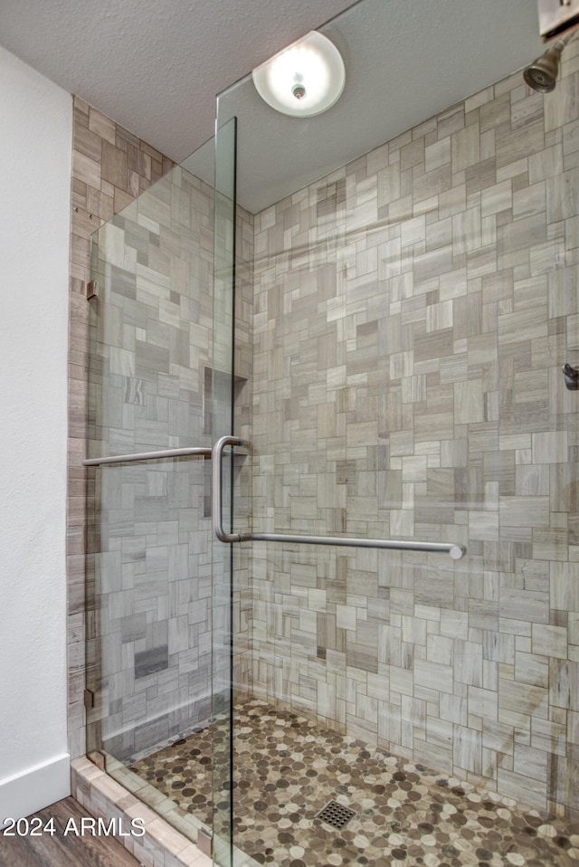 bathroom with a textured ceiling, wood-type flooring, and an enclosed shower