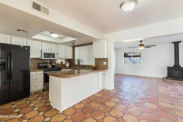 kitchen with kitchen peninsula, tasteful backsplash, black fridge, stainless steel gas stove, and white cabinetry