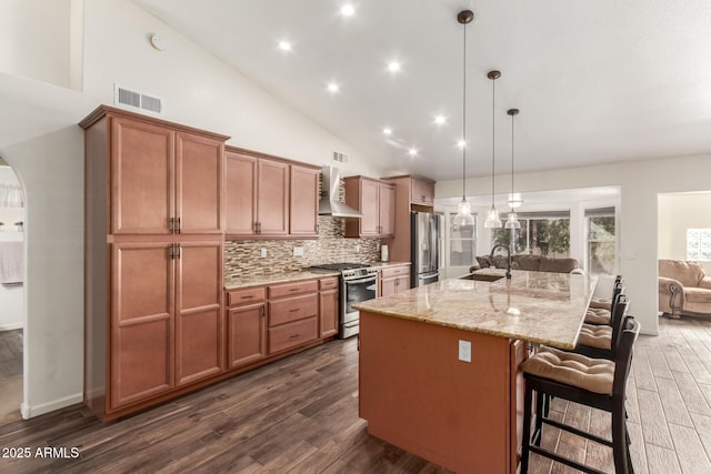 kitchen with a large island, wall chimney range hood, stainless steel appliances, a kitchen breakfast bar, and decorative light fixtures