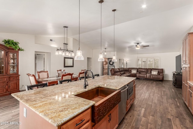 kitchen with light stone counters, stainless steel dishwasher, decorative light fixtures, and a kitchen island with sink