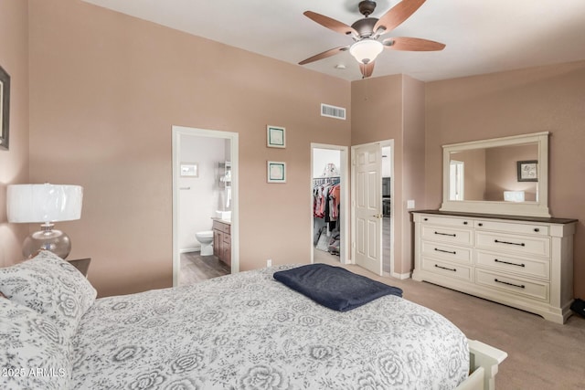 carpeted bedroom featuring a spacious closet, ensuite bath, a closet, and ceiling fan