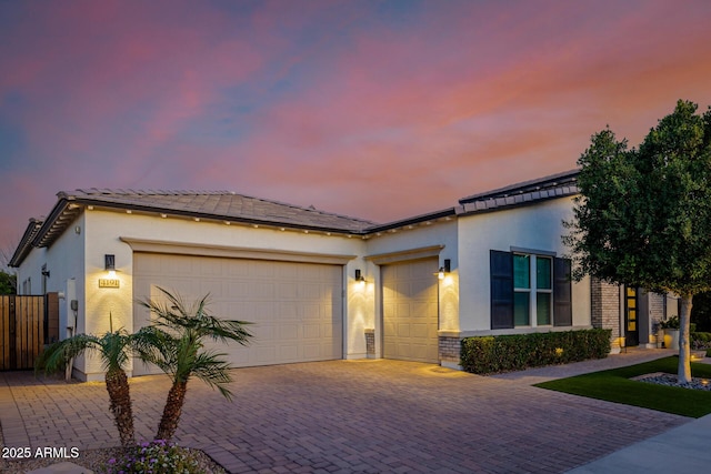 view of front of house with decorative driveway, an attached garage, and stucco siding