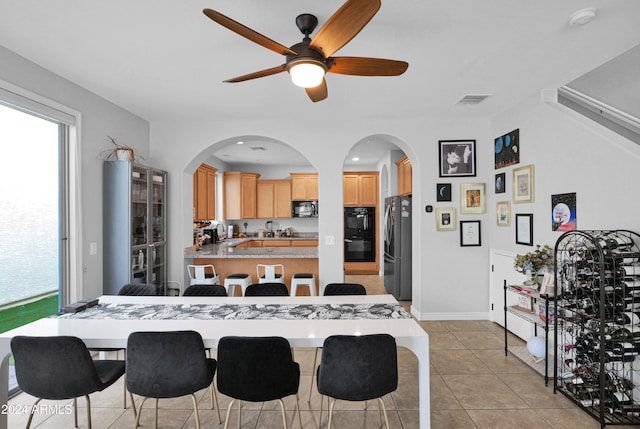 kitchen featuring light tile patterned flooring, kitchen peninsula, a breakfast bar area, black appliances, and light brown cabinets