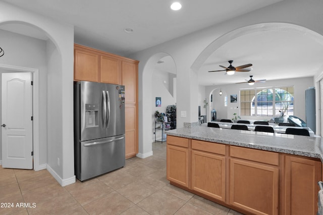 kitchen featuring ceiling fan, stainless steel fridge, light stone countertops, and light tile patterned floors