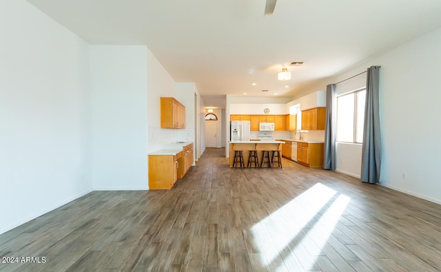 kitchen featuring a center island, white appliances, sink, hardwood / wood-style flooring, and a breakfast bar area