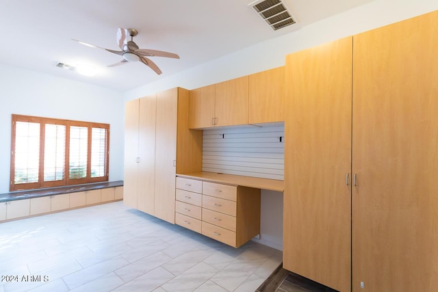 interior space featuring light brown cabinets, built in desk, and ceiling fan