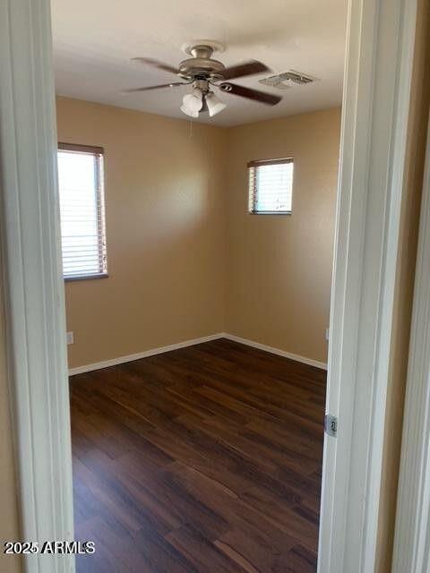 unfurnished room with dark wood-style floors, visible vents, baseboards, and a ceiling fan