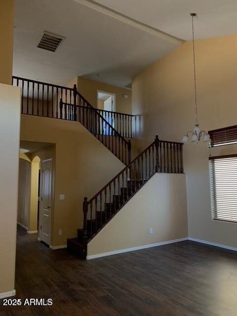 stairway featuring visible vents, a high ceiling, wood finished floors, a chandelier, and baseboards