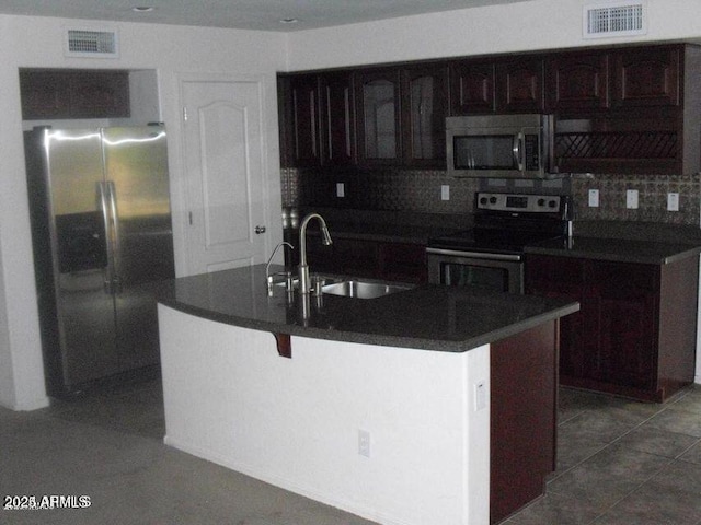 kitchen featuring visible vents, dark countertops, a kitchen island with sink, stainless steel appliances, and a sink