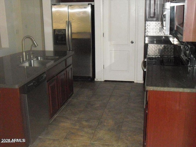 kitchen with dark countertops, appliances with stainless steel finishes, a kitchen island with sink, dark tile patterned floors, and a sink