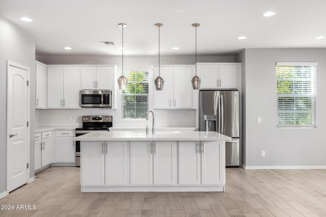 kitchen with hanging light fixtures, light hardwood / wood-style flooring, an island with sink, appliances with stainless steel finishes, and white cabinetry