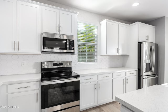 kitchen with light stone countertops, appliances with stainless steel finishes, light wood-type flooring, tasteful backsplash, and white cabinets