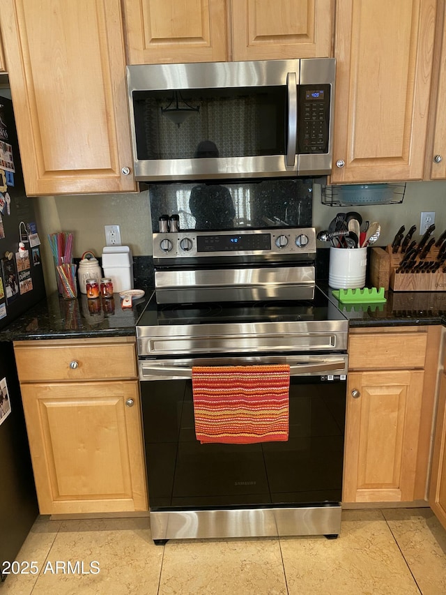 kitchen featuring stainless steel appliances, light tile patterned flooring, and dark stone counters