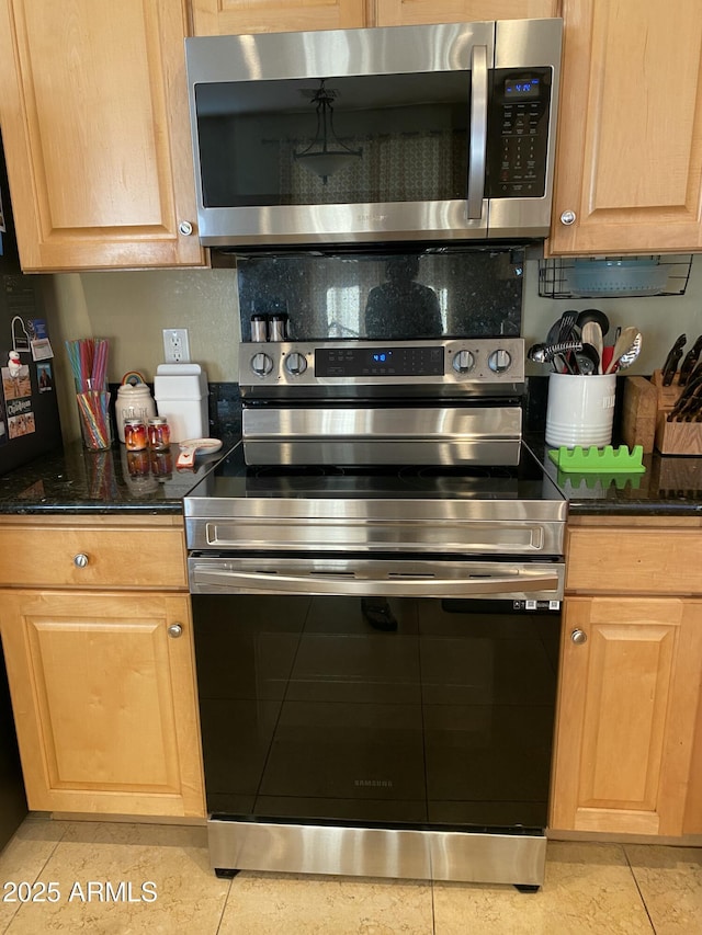 kitchen with light tile patterned floors, dark stone counters, and appliances with stainless steel finishes