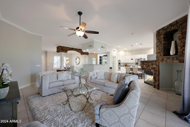 tiled living room featuring crown molding, a stone fireplace, and ceiling fan