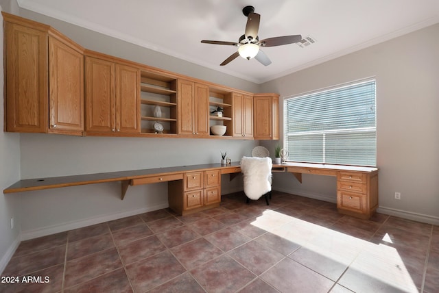 unfurnished office with ornamental molding, built in desk, dark tile patterned floors, and ceiling fan