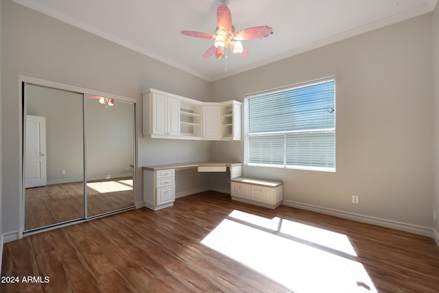 unfurnished bedroom with built in desk, a closet, ceiling fan, ornamental molding, and dark hardwood / wood-style floors