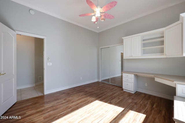 unfurnished office with built in desk, crown molding, dark hardwood / wood-style floors, and ceiling fan