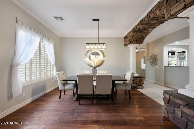 dining area featuring dark wood-type flooring, crown molding, and decorative columns