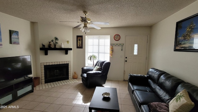 living room with ceiling fan, a textured ceiling, a tile fireplace, and light tile patterned floors