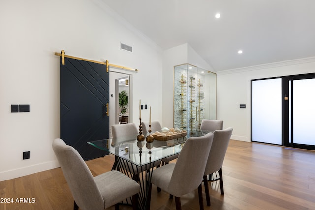 dining space featuring hardwood / wood-style floors, a barn door, crown molding, and lofted ceiling