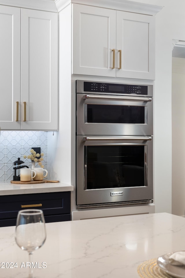 kitchen featuring decorative backsplash, white cabinetry, stainless steel double oven, and light stone counters