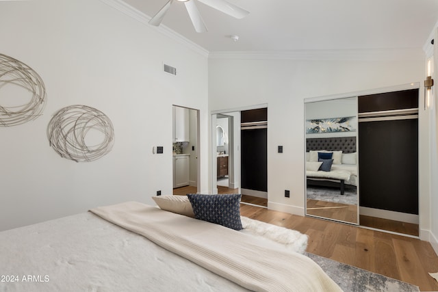 bedroom with high vaulted ceiling, two closets, hardwood / wood-style flooring, ceiling fan, and ornamental molding