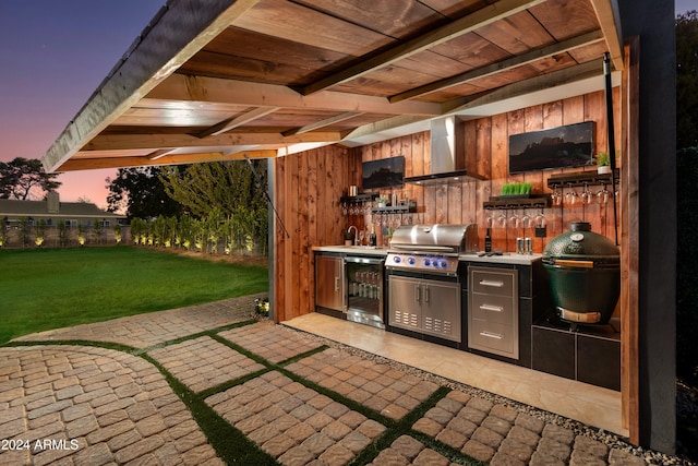 patio terrace at dusk with area for grilling, a yard, and an outdoor kitchen