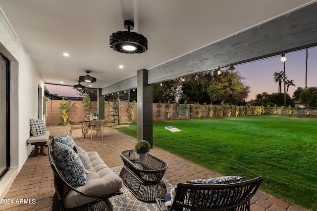 patio terrace at dusk featuring outdoor lounge area, ceiling fan, and a lawn