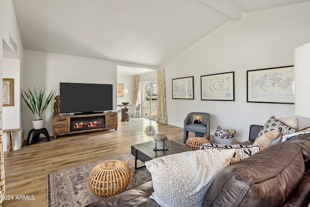 living area with baseboards, visible vents, a glass covered fireplace, wood finished floors, and vaulted ceiling with beams