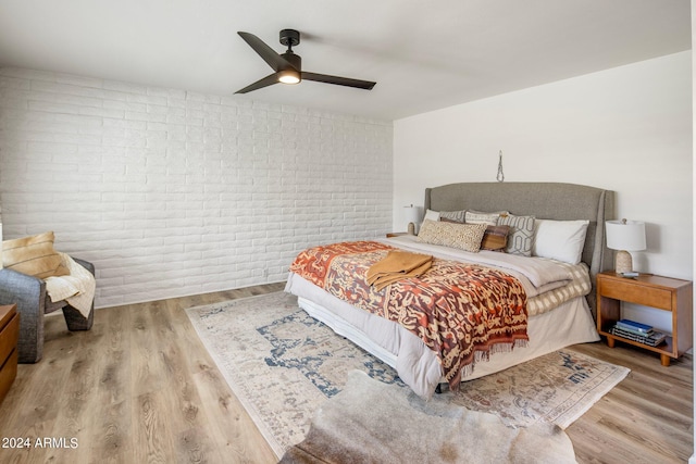 bedroom with ceiling fan, brick wall, and wood finished floors