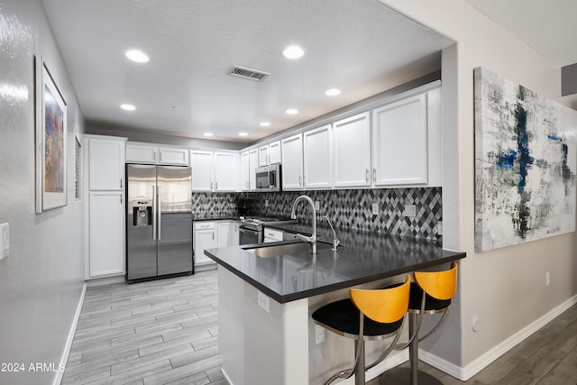 kitchen featuring appliances with stainless steel finishes, white cabinets, sink, a breakfast bar area, and kitchen peninsula