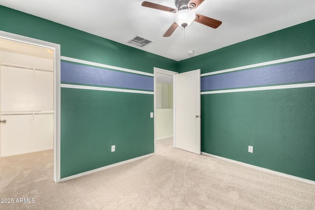 unfurnished bedroom featuring light carpet, a walk in closet, a closet, and ceiling fan