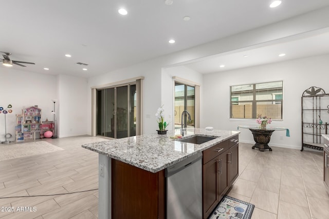 kitchen featuring dishwasher, an island with sink, sink, ceiling fan, and light stone counters