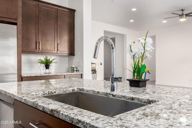 kitchen featuring sink, decorative backsplash, dark brown cabinets, and light stone countertops