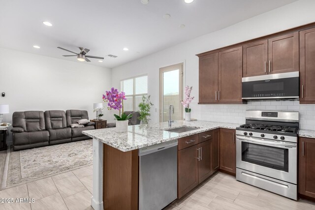 kitchen featuring sink, appliances with stainless steel finishes, light stone counters, decorative backsplash, and kitchen peninsula