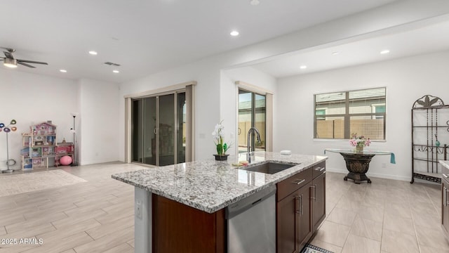 kitchen with sink, light stone counters, dishwasher, ceiling fan, and a kitchen island with sink