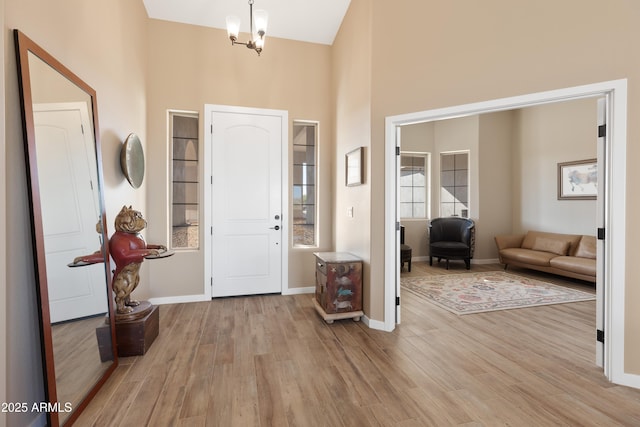 entrance foyer featuring light wood-style floors, a high ceiling, baseboards, and an inviting chandelier