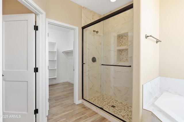 bathroom with a tub to relax in, a walk in closet, a marble finish shower, and wood tiled floor